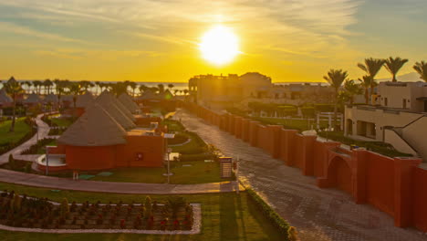 Sunrise-over-a-tropical-resort-with-palm-trees-and-thatched-roofs,-timelapse-of-daybreak