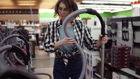 pretty curly haired woman standing near new vacuum cleaners in home appliance store, take one to compare. various vacuum