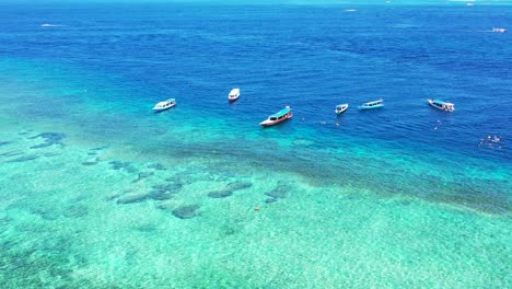 Fishing-Boats-In-Indonesia-Anchored-In-The-Deep-Blue-And-Shallow-Light-Blue-Sea-Water-During-Summer---Aerial-Shot