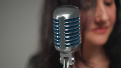 primer plano de una vocalista femenina borrosa moviendo suavemente la cabeza frente a un micrófono vintage contra un fondo de enfoque suave