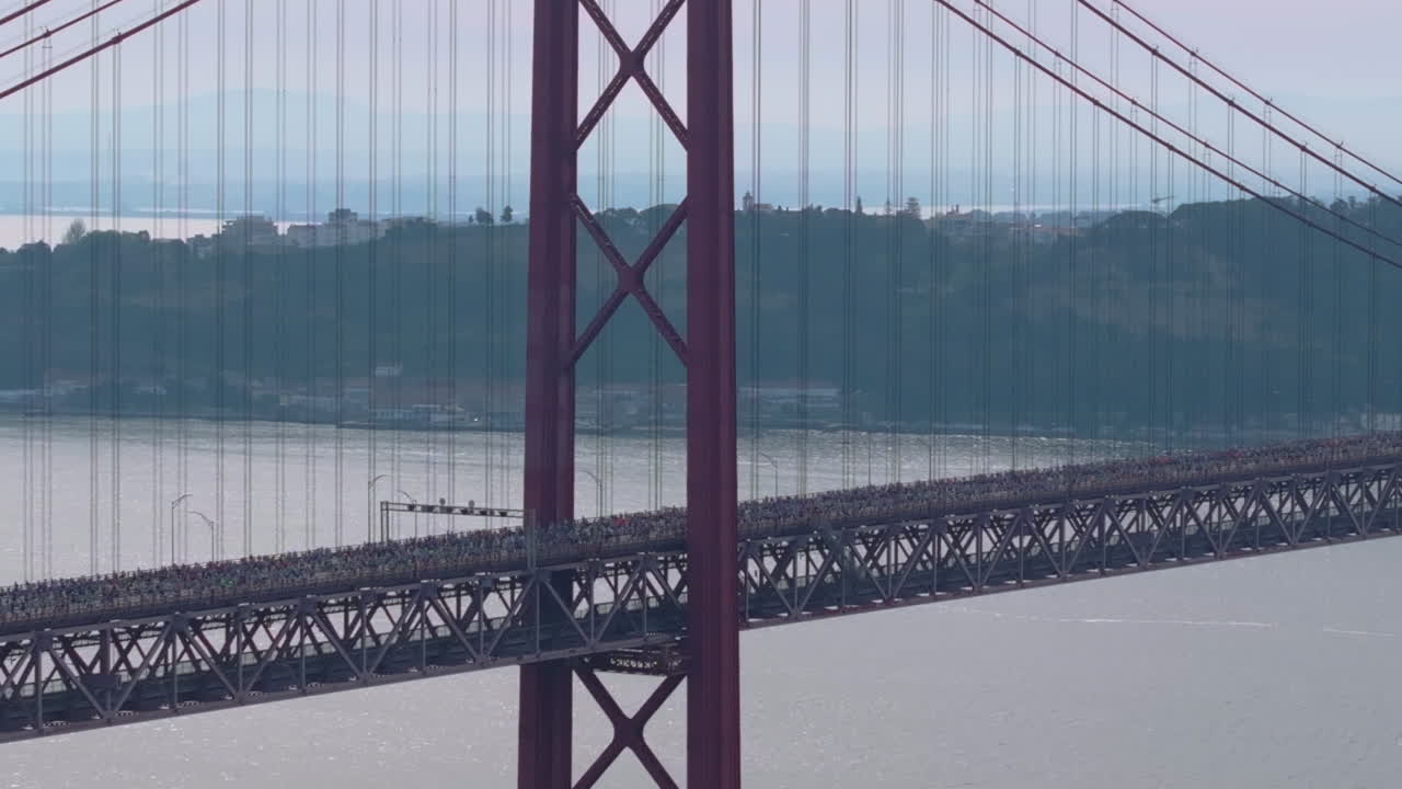 Half marathon and 10K long distance running event in Lisbon, Portugal, Europe. Runners crossing the iconic famous red 25th April suspension bridge. Cinematic sports aerial drone shot