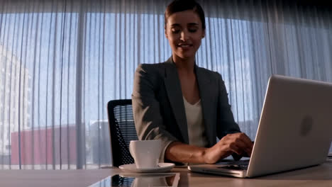 female business executive having coffee while using laptop