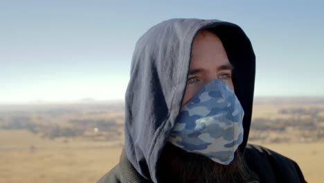 man removing his mask then takes a deep breath on top of a mountain