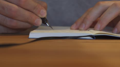 man writing with fountain pen in a notebook on a table