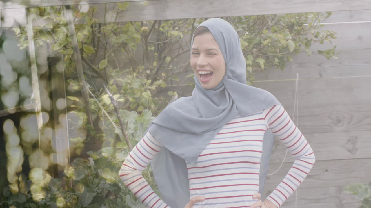 Animation of leaves over biracial woman in hijab smiling