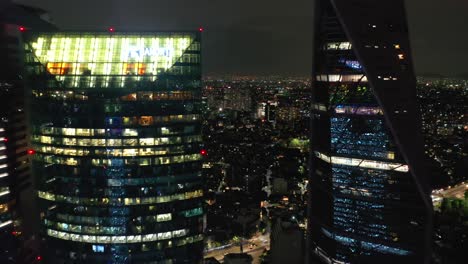 exhilarating high aerial flight through narrow opening between tall torre mayor tower skyscraper and reforma glass building lit with pride colors at night, mexico city, drone going away