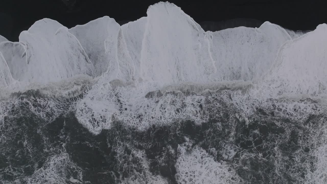Aerial top view over ocean waves crashing on Iceland S&oacute;lheimasandur black sand beach