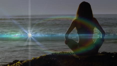 Animation-of-light-spots-over-caucasian-woman-practicing-yoga-and-meditating-at-beach