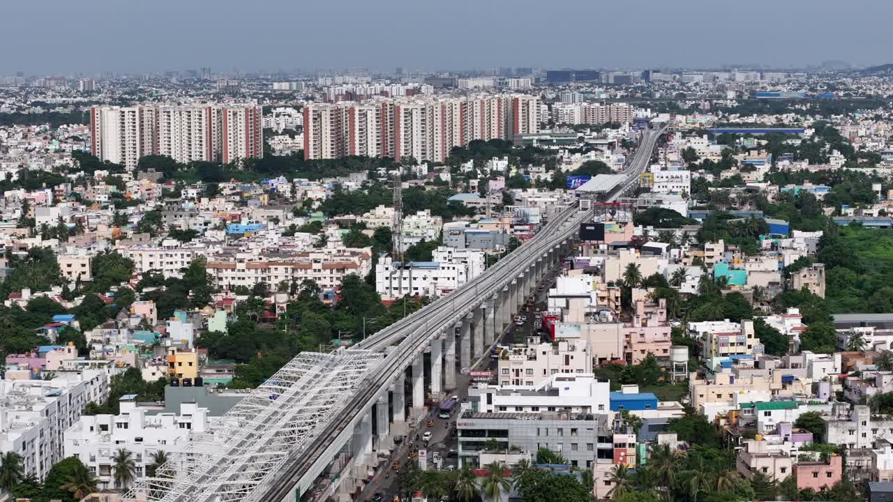 Aerial shot of Chennai's elevated metro line cutting through dense residential areas and towering high-rise apartments. Classic Indian urban sprawl meets modern transit infrastructure