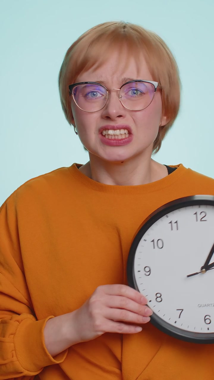Femme aux lunettes avec anxiété vérifiant l'heure sur l'horloge en retard au travail en retard sur la date limite
