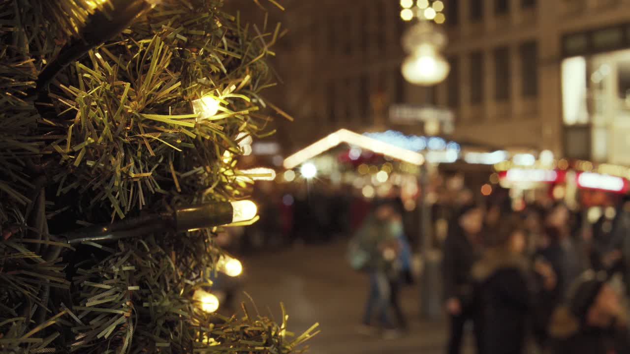 Gefocust op een dennentak met lichtjes op een volle kerstmarkt met wazige mensen op de achtergrond
