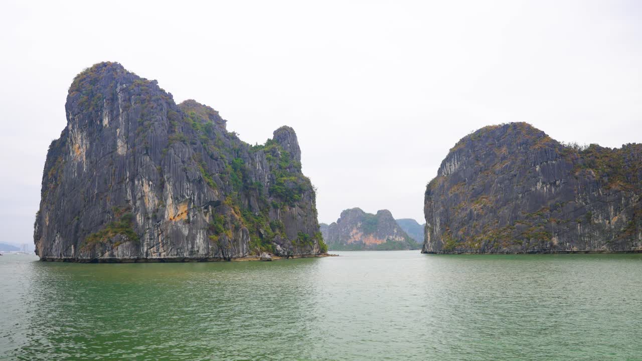 Towering limestone karsts rise dramatically from the emerald waters of Ha Long Bay, cliffs draped in sparse vegetation, creating a mystical seascape that showcases Vietnam's most iconic natural wonder