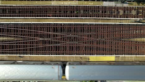 a top down view, directly above elevated train tracks as a silver subway travels from left to right of the frame on a sunny day