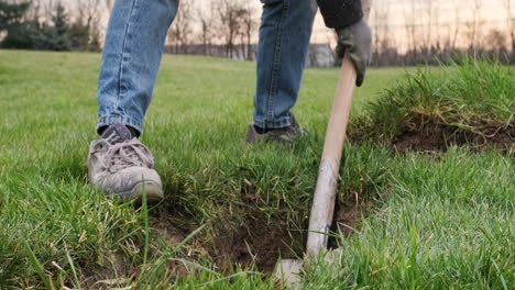 man gardener digging soil with shovel making a hole on the ground with meadow landscape during winter. - close up shot