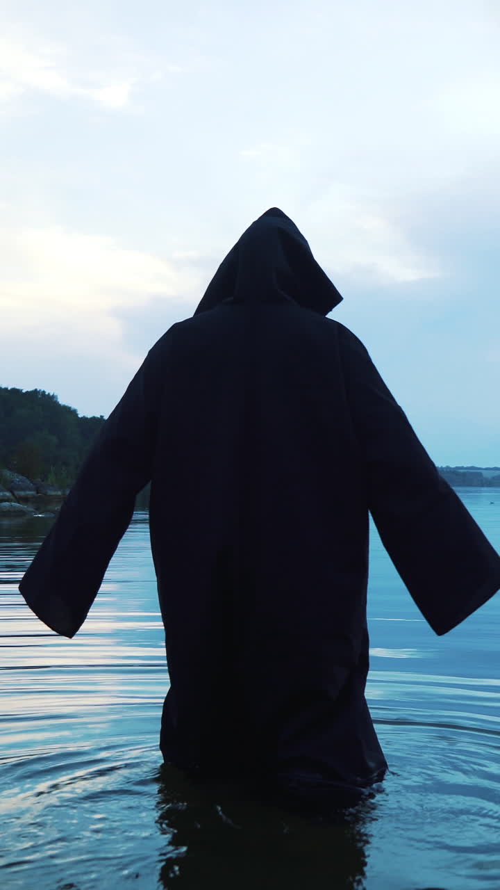 Scary figure in black mantle in the river.. Vertical video