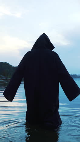 scary figure in black mantle in the river.. vertical video