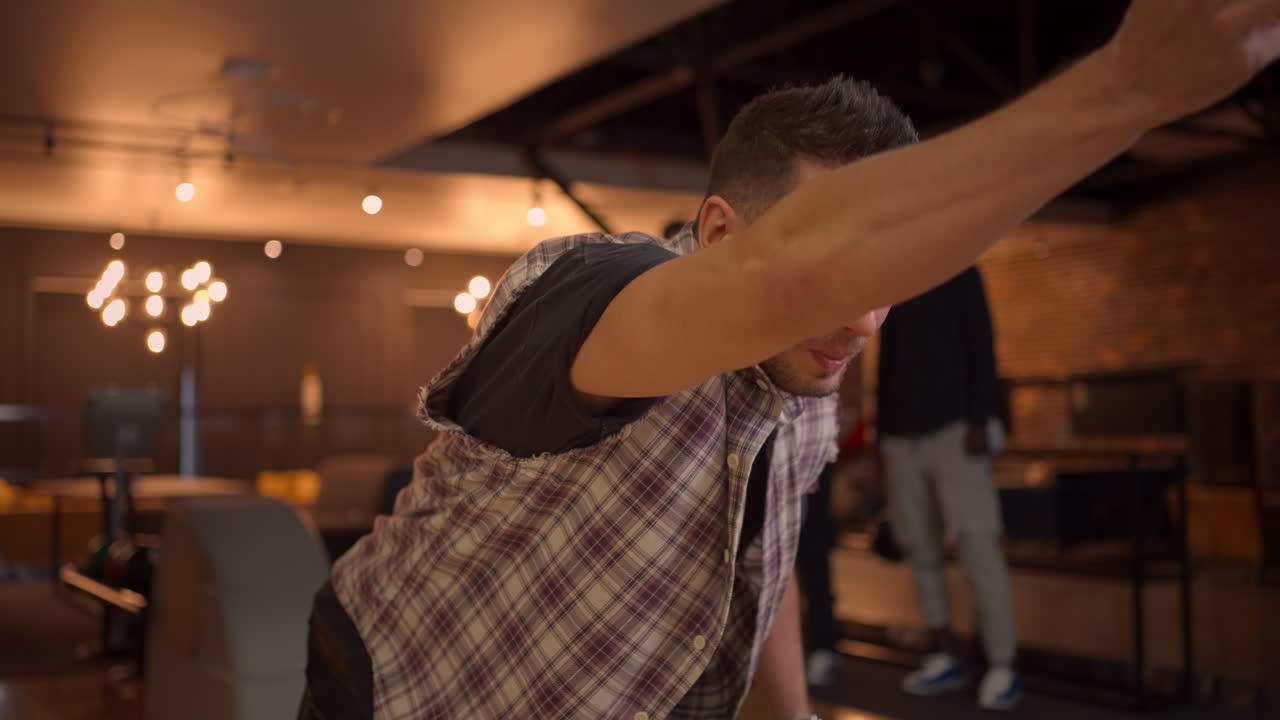 A portrait of a Caucasian man throws a bowling ball and knocks out a shot with one throw. Multi-ethnic group of friends bowling