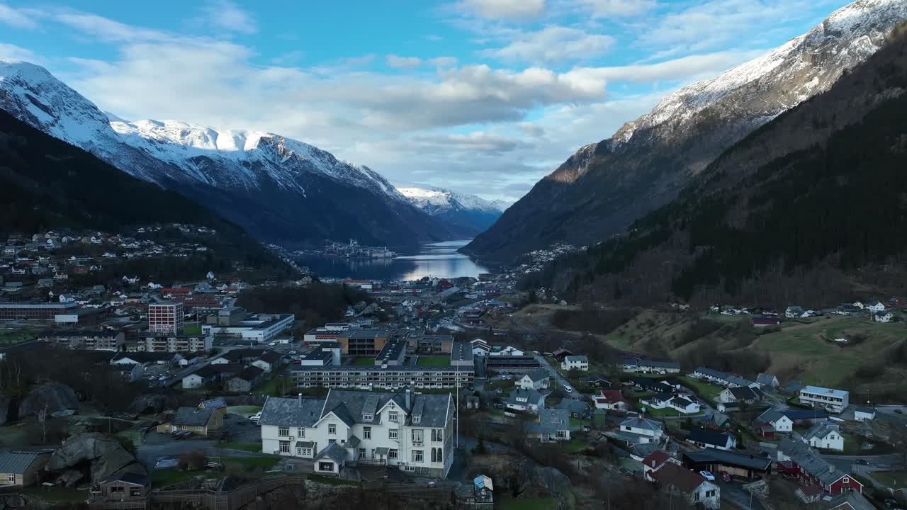 Odda Norway at sunset with Sorfjorden, cityscape, and sunlit mountains, descending aerial
