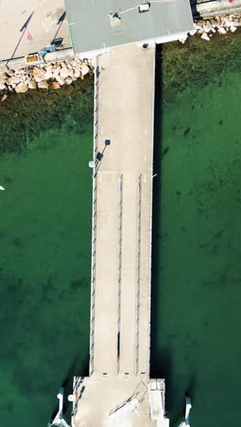 vertical, aerial: nyon wharf with green and blue lake of geneva during the day in canton of vaud, switzerland, top down drone shot