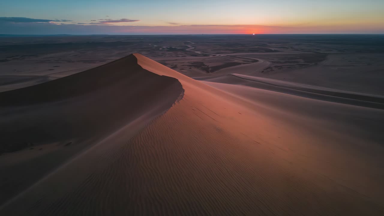 Drone che scivola lungo la cresta di una duna sopra il deserto mentre il sole tramonta, rivelando increspature e un bordo illuminato dal sole