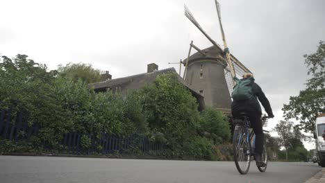 Eine-Junge-Holländerin-Radelt-An-Einer-Alten-Windmühle-Vorbei