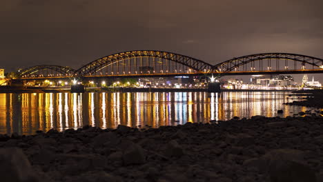 south-bridge in cologne over the rhine river in central cologne. night time lapse video. beautiful reflections in the water. train and boat traffic, light trails. smooth camera slide.