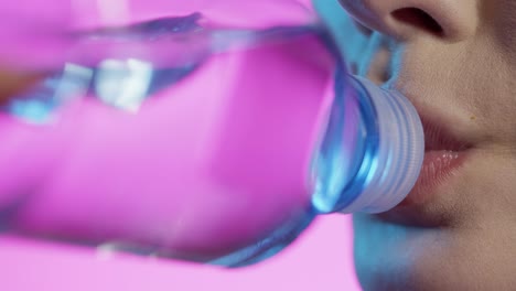 woman-sipping-water-from-waterbottle-in-close-up,-girly-nail-polish-and-red-lipstick-lips-on-pink-background