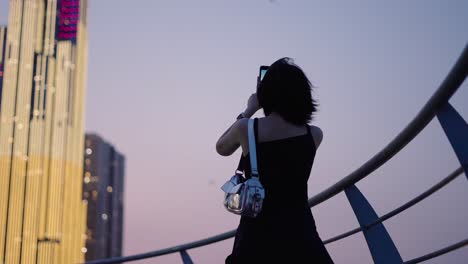Woman taking photo of a city skyline at dusk