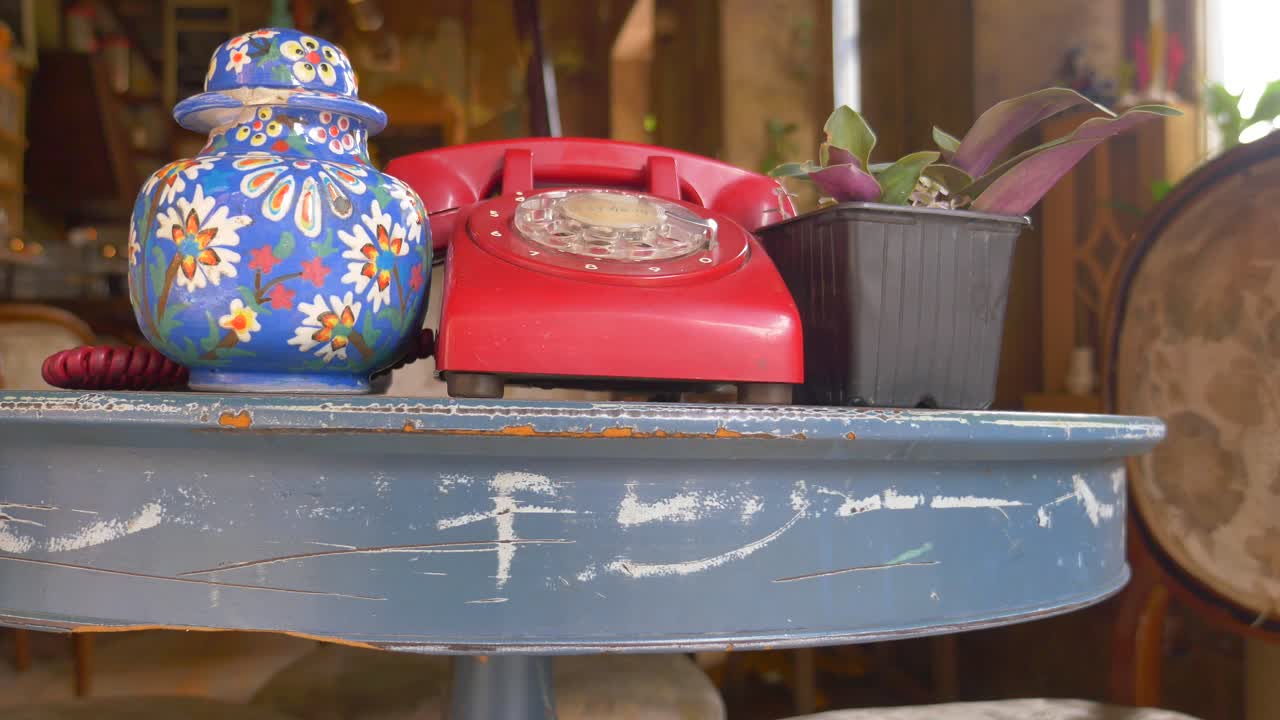 파란 테이블 위의 빈티지 빨간 회전 전화기와 칠한 꽃병과 식물