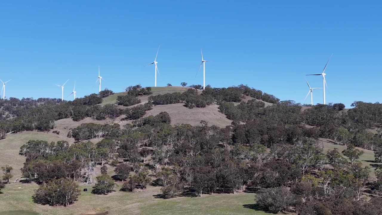 Drone ascende sobre colinas verdes ondulantes em direção a turbinas eólicas modernas na zona rural de Nova Gales do Sul