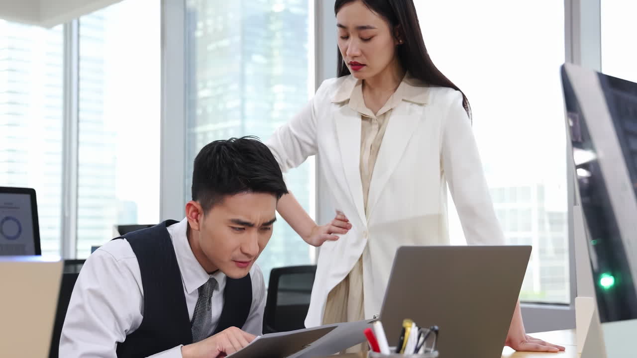 緊迫したオフィスで、厳格な上司が反省している部下を叱責する。上司は部下の仕事ぶりに不満を抱き、厳しい業務規定を理由に叱り、非難している。