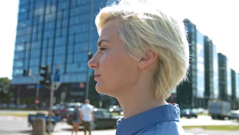 confident, young, blonde, woman staring intently off into the distance of a big city wearing a blue collared shirt with hair blowing in the wind and traffic passing in the blurred background