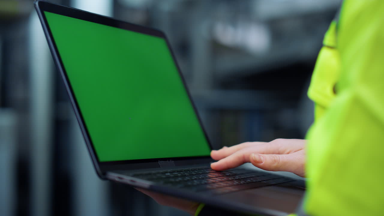 laptop de pantalla verde en primer plano. manos especializadas escribiendo en la computadora de la fábrica.