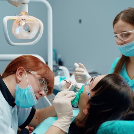 female patient visits stomatologist. dentist and assistant in mask and safety glasses treating client's tooth in dental cabinet. tooth treatment.