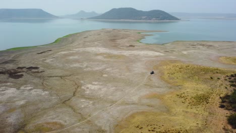 Aerial-drone-shot-of-an-off-roading-jeep-exploring-a-dried-up-lake-reservoir-at-harsi-dam-in-gwalior-india