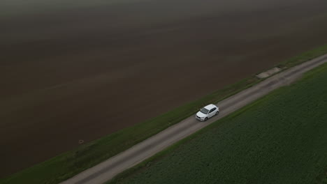 white car driving country road between fields, following revealing drone view, bad cloudy weather and fog