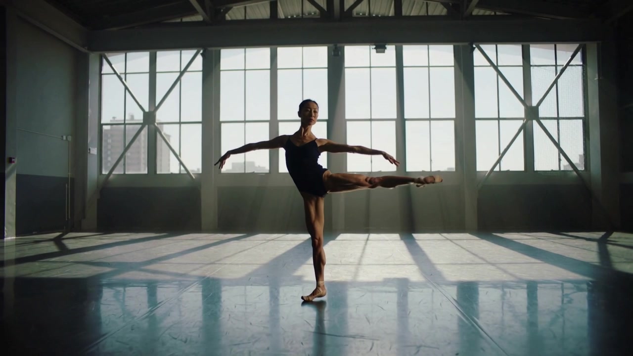 Starting phrase, dancer rehearsing side lift in sunlit studio in dark leotard, ballet shoes