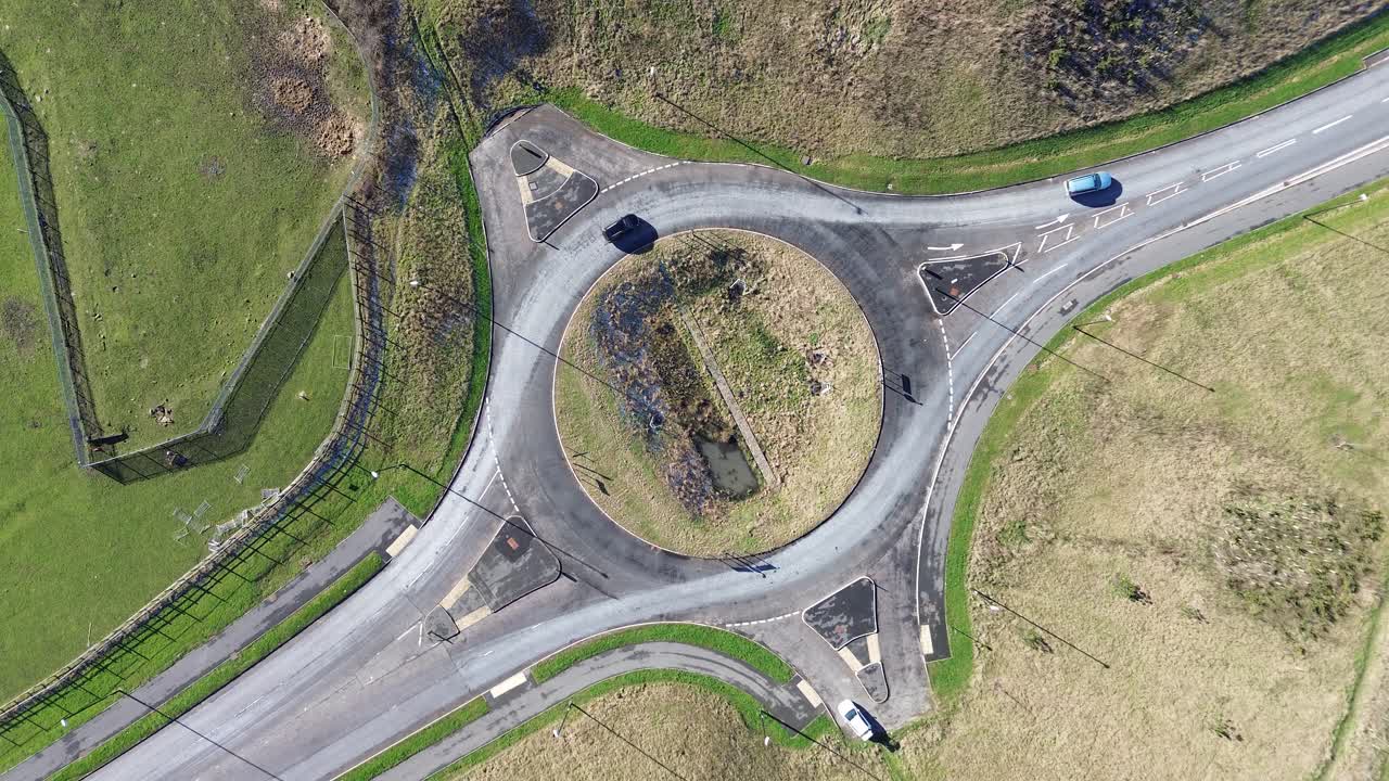 Unfinished roundabout from above with two incomplete junctions as two cars drive across. Drone top-down traffic movement, roadworks, infrastructure, countryside roads