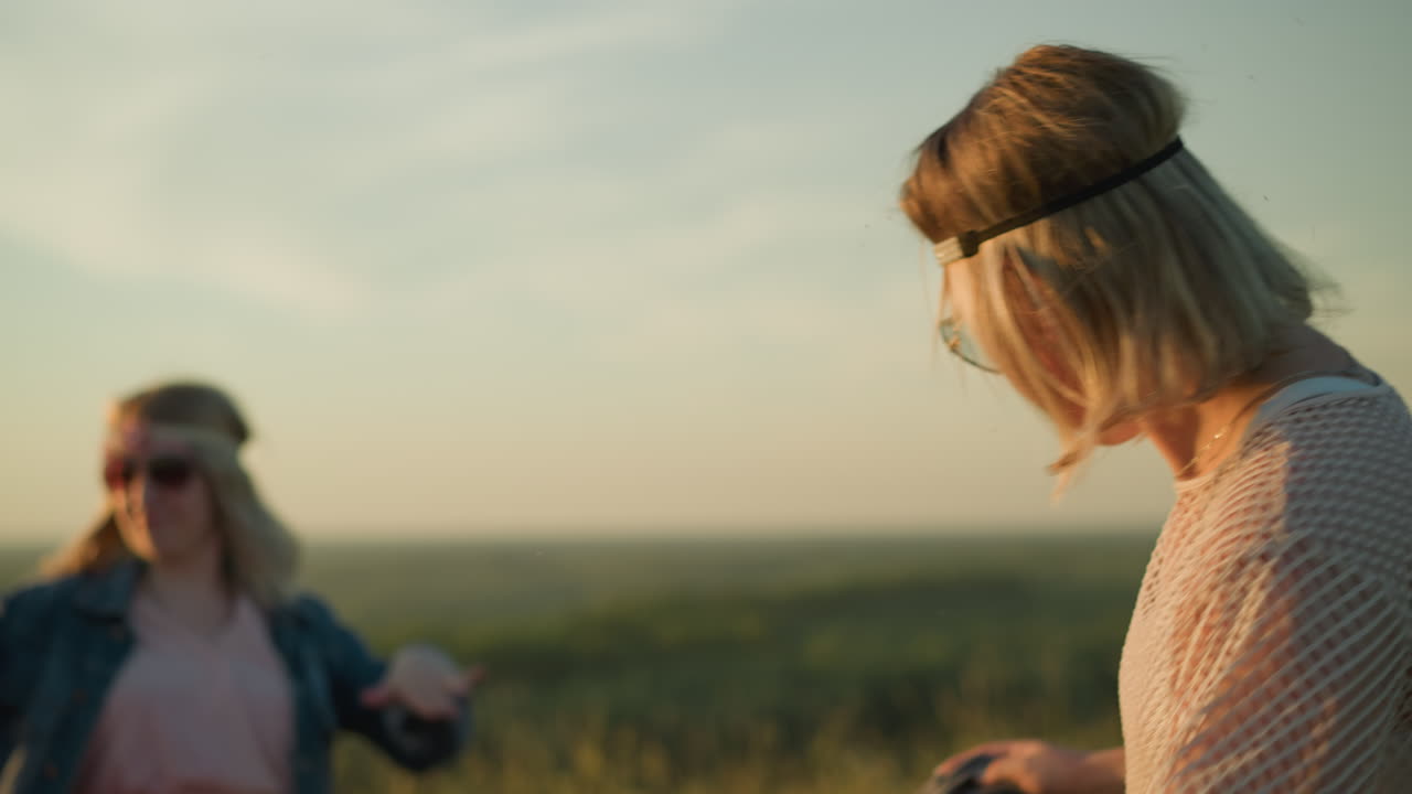 두 명의 즐거운 여성들이 잔디에 있는 빨간 모터사이클 근처에서 춤을 추고 있습니다. 그들은 야외에서 축하하고 시간을 즐기고 있습니다.