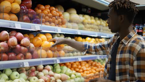 stylish guy choosing oranges while shopping in big shop