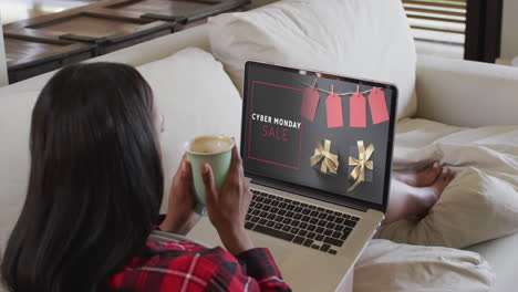 una mujer biracial usando una computadora portátil en casa comprando en línea en el día de venta del lunes cibernético, en cámara lenta