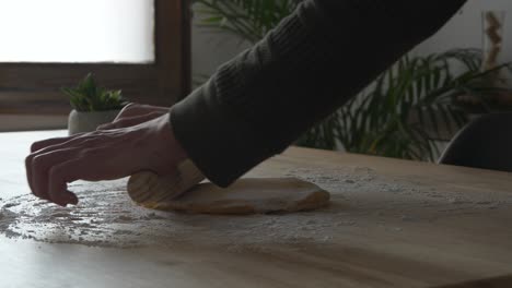 Manos-Del-Hombre-Trabajando-En-Esparcir-Masa-De-Pasta-Con-Un-Rodillo-Sobre-Una-Mesa-De-Madera-Con-Harina-Encima