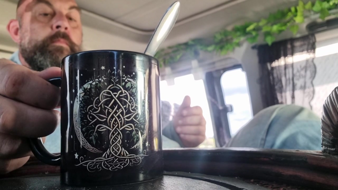 Bearded man in campervan eating quick and easy meal from black cup enjoying views and freedom