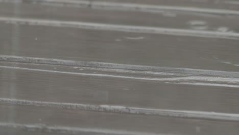 slow motion: raindrops hitting wooden terrace splashing, forming puddles and ripples, droplets exploding into the air