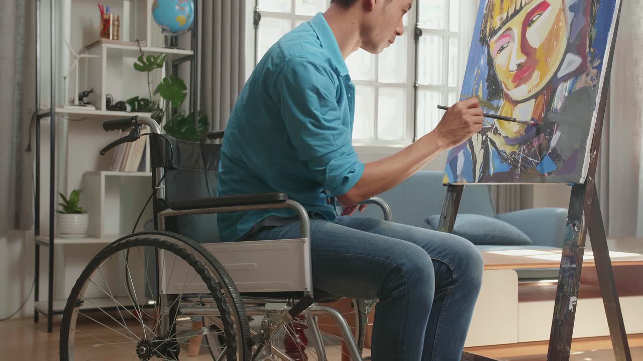 vista lateral de un artista asiático en silla de ruedas sosteniendo un pincel de colores mixtos y pintando a una chica en el lienzo
