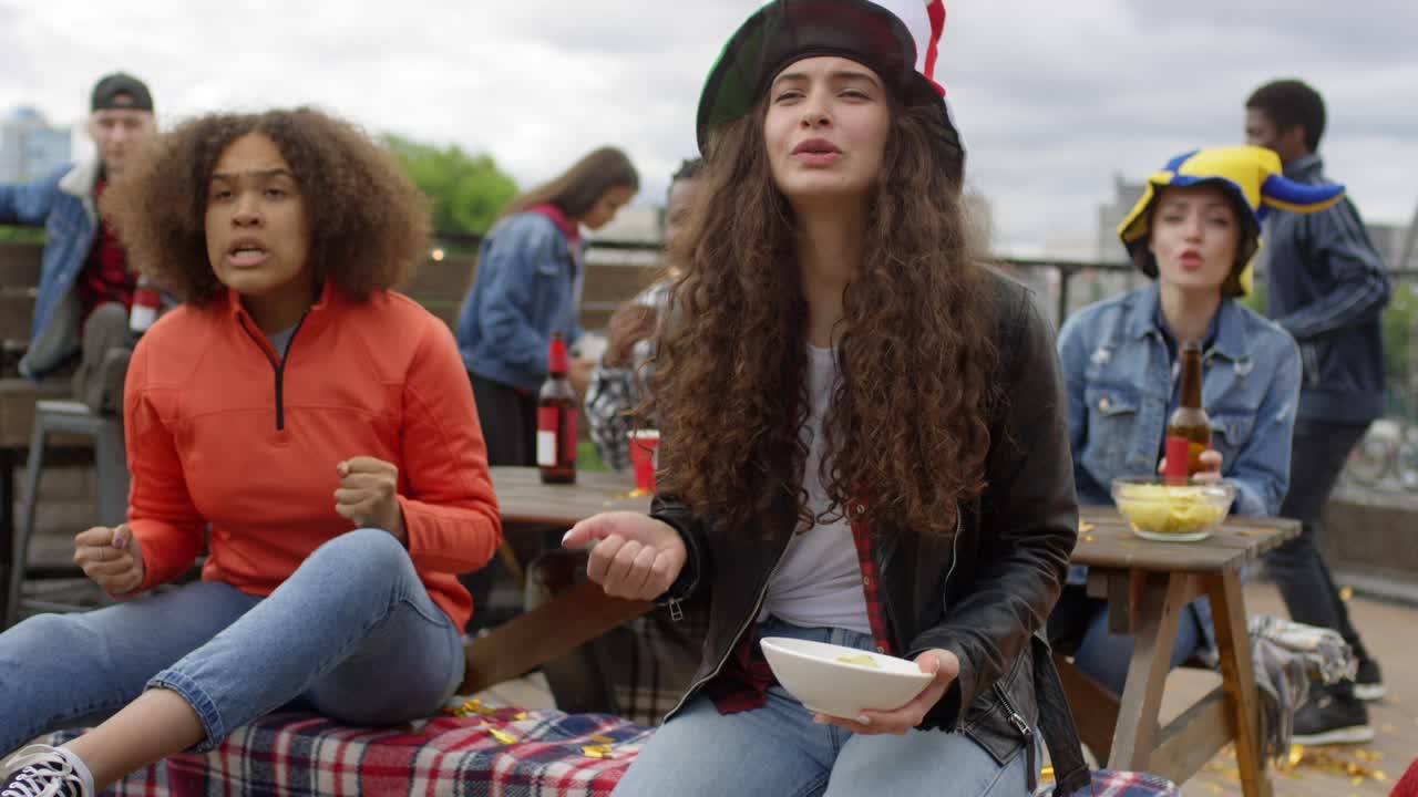 emocionados fanáticos de los deportes masculinos y femeninos viendo el partido, animando al equipo y luego gritando y celebrando el gol bajo la ducha de confeti en el bar al aire libre en la azotea urbana