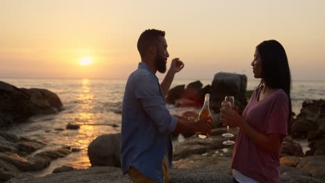 pareja de razas mixtas tomando champán mientras están de pie en una roca en la playa 4k