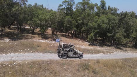 israel army infantry squad soldiers on humvee vehicle driving through green field at training ground country road, aerial tracking shot