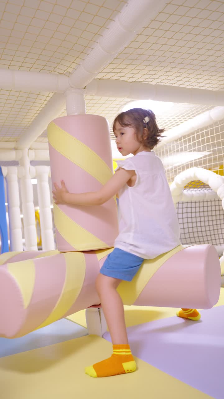 A five-year-old girl happily spins riding on pastel marshmallow-shaped soft play elements at an indoor playground