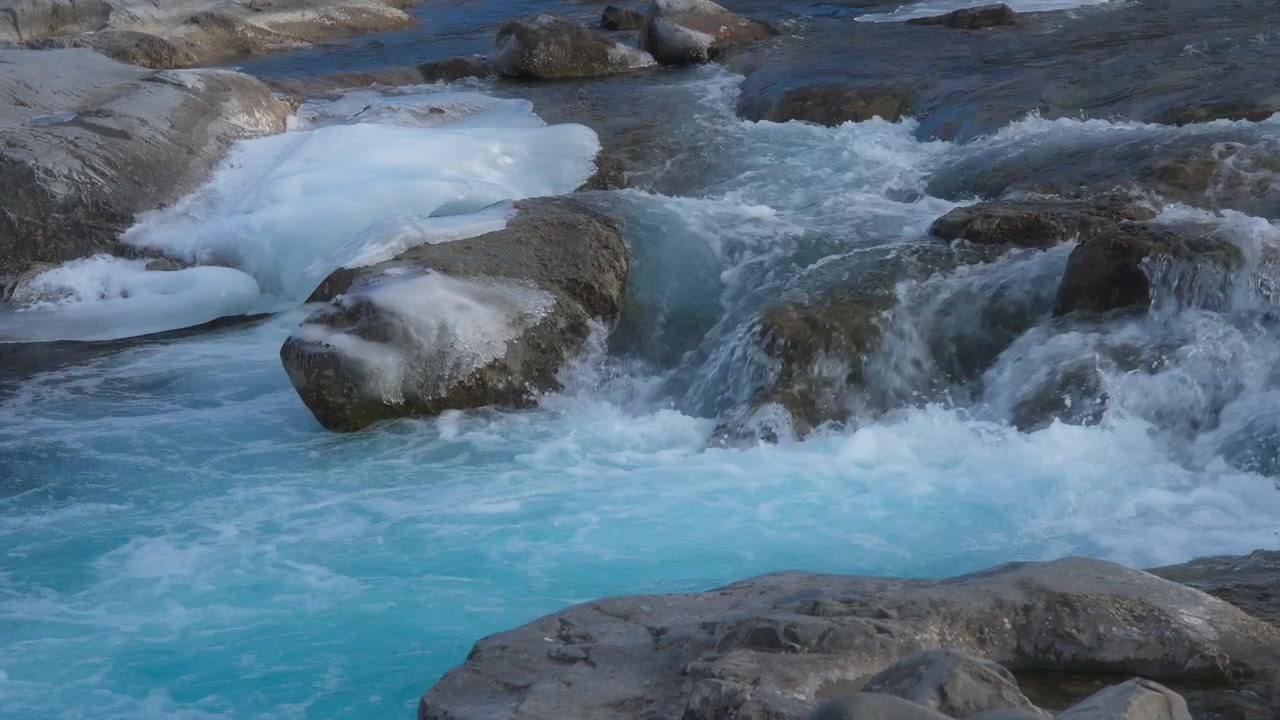 Acqua che scorre a cascata tra le rocce con pezzi di ghiaccio accanto